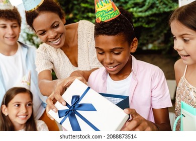 Black Boy Smiling While Opening Gift Box During Birthday Party Outdoors