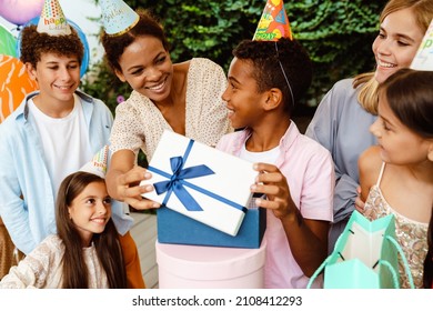 Black Boy Smiling While Opening Gift Box During Birthday Party Outdoors