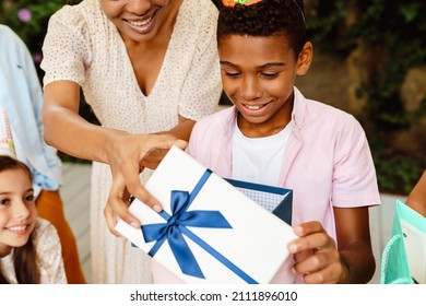 Black Boy Smiling While Opening Gift Box During Birthday Party Outdoors