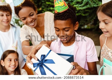 Black boy smiling while opening gift box during birthday party outdoors