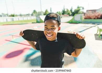 A black boy with black t-shirt posing with his skateboard with the sky in the background - Powered by Shutterstock