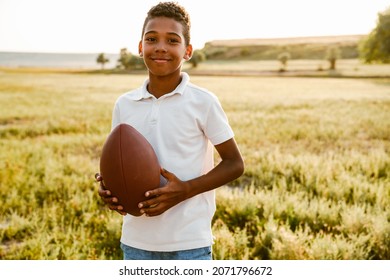 Black boy wearing white shirt smiling while posing with rugby ball outdoors - Powered by Shutterstock