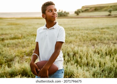 Black boy wearing white shirt posing with rugby ball outdoors - Powered by Shutterstock