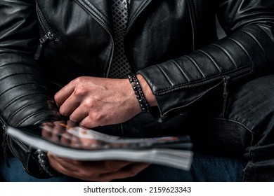 A black bracelet made of expensive stones on a man's hand, a leather jacket and a magazine