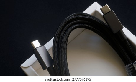Black braided USB-C cable resting in a white packaging box on a dark background. Perfect for modern gadget unboxing, tech retail, and device charging concepts. Photo