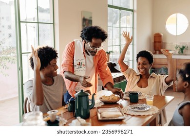 Black Brazilian family bonding over a delicious breakfast meal at home. Father serving pão de queijo, cheese bread rolls, to his excited wife and children. Family spending quality time in the kitchen. - Powered by Shutterstock