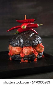 Black Bread Hamburger With Meatballs And Spicy Tomato Sauce On A Black Plate And Table. Low Light Strange Burger Image. Weird Food. Halloween Dish.