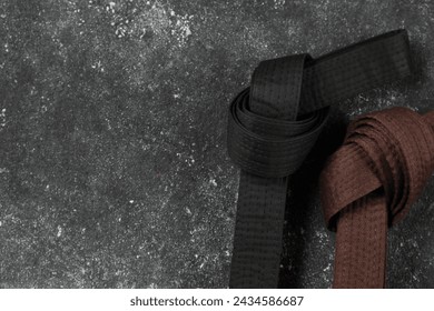 Black and brown karate belts on gray textured background, flat lay. Space for text