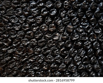 Black bubble wrap for packing, shipping, or security packaging to cushion breakable or valuable items during transport. The material has a dense pattern of air-filled bubbles for protection