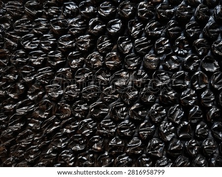 Black bubble wrap for packing, shipping, or security packaging to cushion breakable or valuable items during transport. The material has a dense pattern of air-filled bubbles for protection