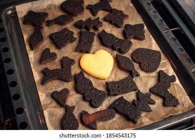 Black Burned Bakery With One White Cookie In The Middle. Christmas Biscuits In Different Shapes On Baking Tray