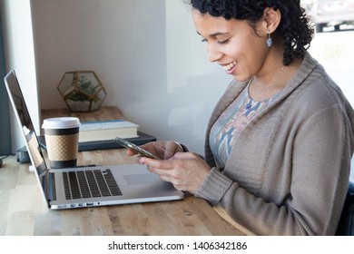 Black business woman works on her phone and computer at work - Shutterstock ID 1406342186