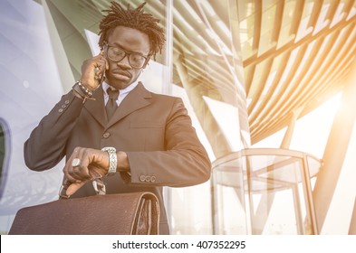 Black businessman delayed checking the time in the watch while he is making a telephone call with his mobile phone - Powered by Shutterstock