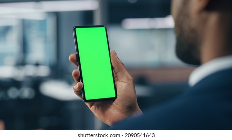 Black Businessman with Green Screen Chroma Key Smartphone in Office. African-American Businessperson using Internet, Social Media, Online Shopping with Mobile Phone Device. Over Shoulder - Powered by Shutterstock