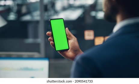 Black Businessman with Green Screen Chroma Key Smartphone in Office. African-American Businessperson using Internet, Social Media, Online Shopping with Mobile Phone Device. Over Shoulder - Powered by Shutterstock