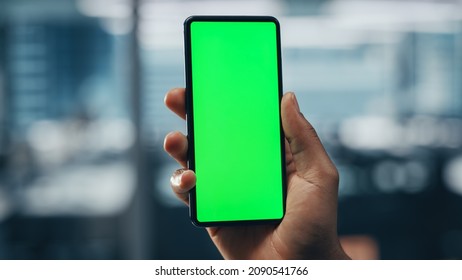 Black Businessman With Green Screen Chroma Key Smartphone In Office. African-American Businessperson Using Internet, Social Media, Online Shopping With Mobile Phone Device. Over Shoulder