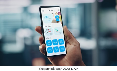 Black Businessman Holding Smartphone With Openned Delivery App In Office. African-American Businessperson Using Mobile Phone Device For Order Food Delivery. Over Shoulder Shot