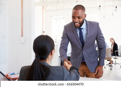 Black businessman and seated woman shaking hands in office - Shutterstock ID 656504470
