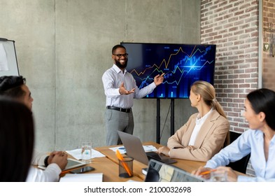 Black Businessman Showing Company Growth On Monitor During Meeting With Colleagues In Office, Group Of Multiethnic Coworkers Looking At Corporate Financial Performance On Screen In Boardroom