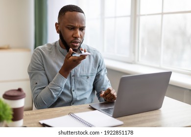 Black Businessman Using Mobile Phone With Voice Assistant Application Or Talking With Loudspeaker Mode Holding Cellphone Near Mouth Sitting In Modern Office. IoT, Voice Search Business App - Powered by Shutterstock