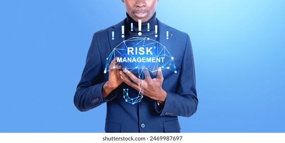 Black businessman using tablet in hands, risk management umbrella hologram with exclamation marks on blue background. Concept of money insurance and business safety - Powered by Shutterstock