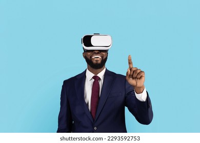 Black Businessman Using VR Glasses And Touching Air With Finger, Happy African American Male Entrepreneur Experiencing Virtual Reality, Enjoying Video Games While Standing On Blue Background - Powered by Shutterstock