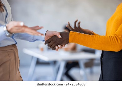 A Black businesswoman and a Caucasian colleague exchange a firm handshake, symbolizing partnership, in the bright, contemporary workspace. They are professionally dressed - Powered by Shutterstock