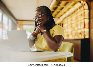 Black businesswoman having a video call with her colleagues while working in a cafe. Mature businesswoman with dreadlocks attending a virtual meeting on a laptop. - Powered by Shutterstock