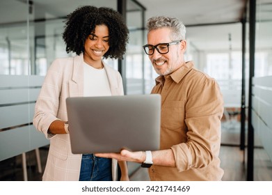 Black businesswoman and her senior male colleague engage warmly with a laptop, discussing strategic ideas or reviewing a presentation, creating a team that values experience and innovation equally - Powered by Shutterstock