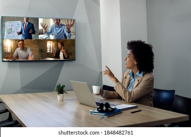 Black businesswoman talking to coworkers via projection screen during video call in the office. 