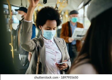 Black Businesswoman Text Messaging On Mobile Phone And Wearing Face Mask While Commuting To Work By Bus. 