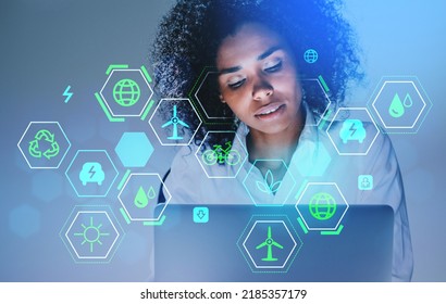 Black Businesswoman Working With Laptop, Pensive Look. Glowing Green Energy Hud With Diverse Icons. Concept Of Technology And Development