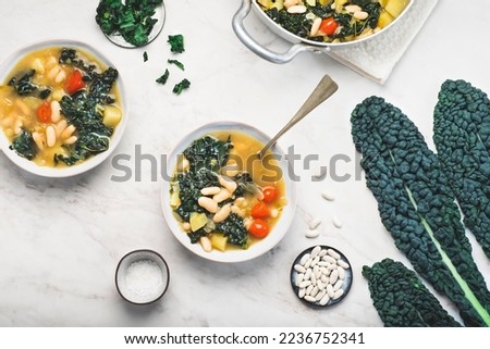 Black cabbage (Toscan kale or cavolo nero) Minestrone soup  with white Cannellini beans on the white background. Italian Tuscan Medici winter recipes. Healthy  tradition vegetarian food, top view