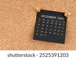 Black calendar sheet for December 2024 with thumbtack on wooden board.