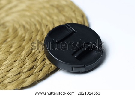 Black camera lens cap on a woven natural mat with a white background