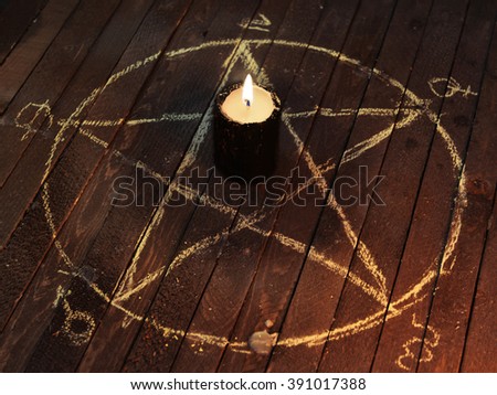 Black candle in pentagram on wooden planks. Magic ritual with occult, evil and esoteric symbols. Scary halloween rite