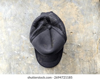 Black cap with mesh back lying on gray concrete floor. This photo captures a simple everyday object with rough texture and natural lighting.