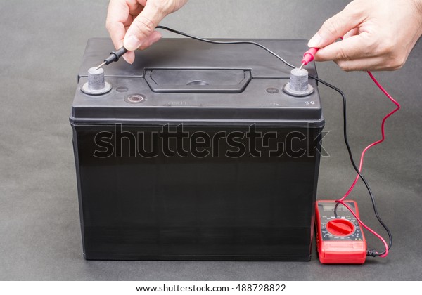 Black car\
battery which measure voltage with a\
tester