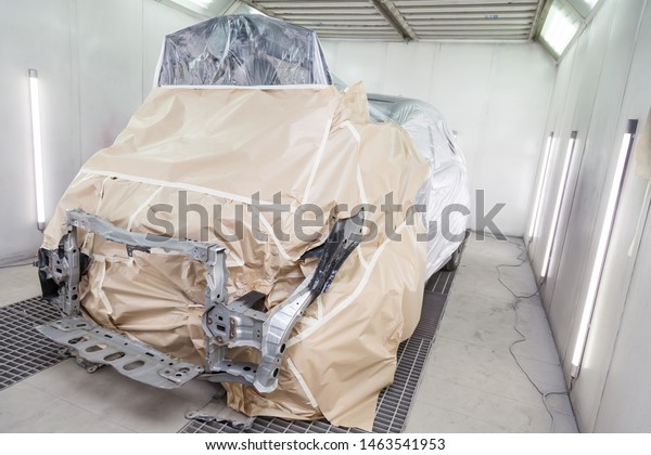 A black car is completely covered in paper and\
adhesive tape to protect against splash during painting and repair\
frame after an accident in a workshop for body repair of vehicles\
with bright lighting
