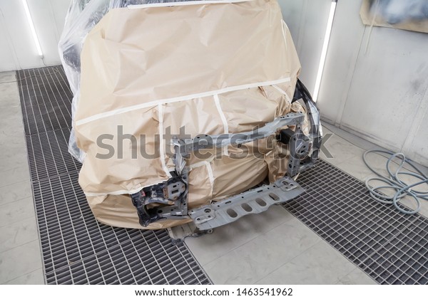 A black car is completely covered in paper and\
adhesive tape to protect against splash during painting and repair\
frame after an accident in a workshop for body repair of vehicles\
with bright lighting