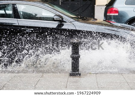 Black car crossing a road and splashing rain water at rainy weather