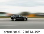 A black car is driving down the street at high speed with a blurred background. Concept of speeding, disobeying traffic rules, dangerous driving.