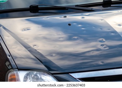 Black car engine hood with many hail damage dents show the forces of nature and the importance of car insurance and replacement value insurance against hail dents of storm hazards extreme weather - Shutterstock ID 2253637403