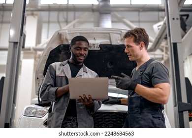 Black Car Mechanic And Caucasian Repairman Checking Diagnostics Results on Laptop, Computer. Explains an Engine Breakdown to Mechanic. Car Service Employees Inspect Car's Engine Bay. Clean Workshop. - Powered by Shutterstock - Get 15% off with code: PIKWIZARD15
