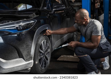 Black car mechanic man checking tire in auto repair workshop, African American car technician working with tire in garage - Powered by Shutterstock