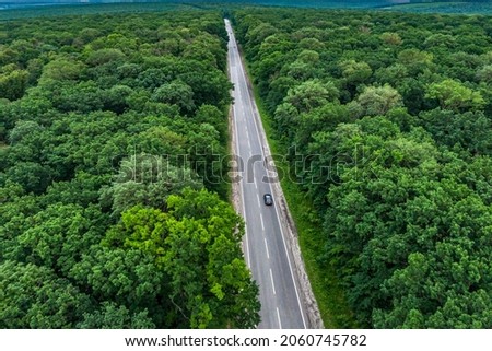 black car on the highway. alone car driving on asphalt road through a green forest. Drone top view seen from the air. Aerial view landscape. drone photography. 
