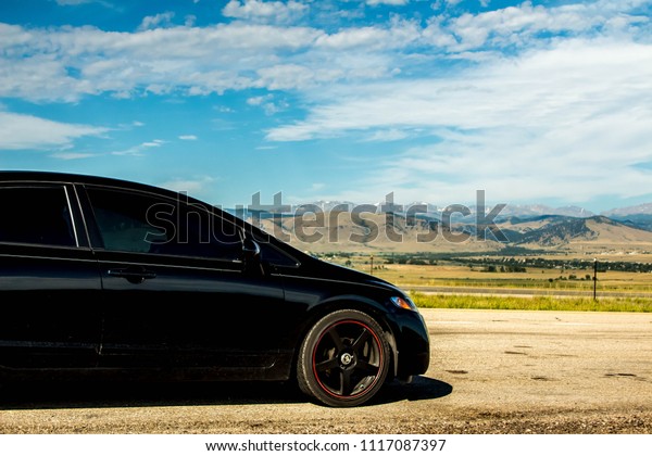 Black car with black rims on clay road looking\
at mountain view\
background