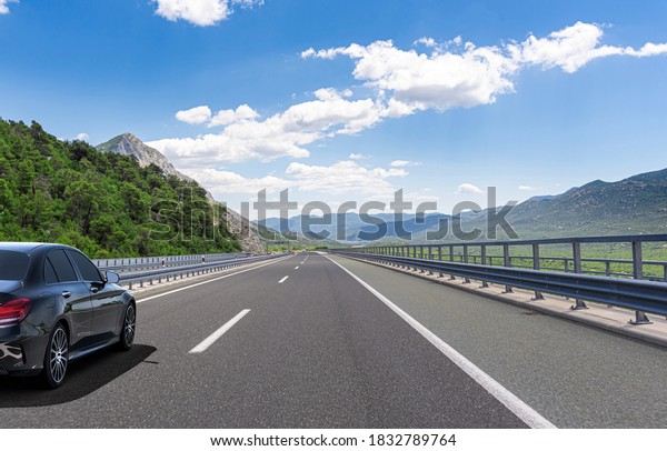 A Black car rushes along the road
against the backdrop of a beautiful countryside
landscape.