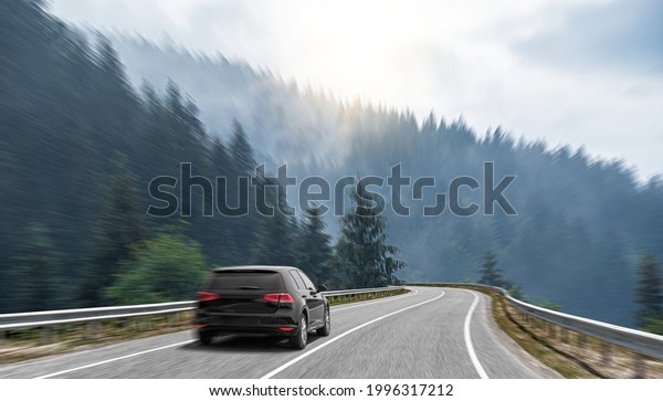 A black car rushes along the road against the
backdrop of a beautiful
landscape.