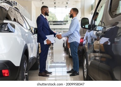 Black Car Seller Shaking Hands With Customer In Modern Dealership Center, Salesman Handshaking With Client After Successful Deal, Selling New Auto To African American Man In Automobile Showroom